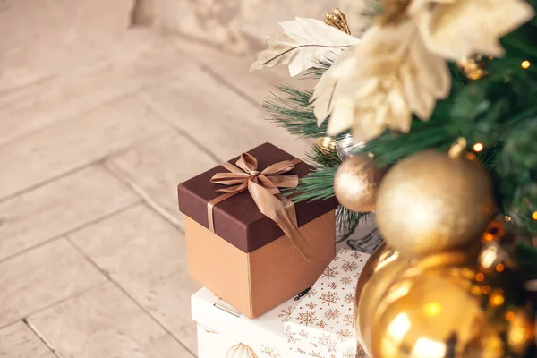 Noel hediyesi kutusu, altın oyuncaklar, toplar ve çelenklerle süslenmiş Noel ağacının altında yerde yatıyor..