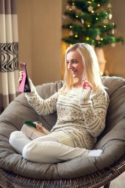 İnternetteki Noel ve yeni yıl kutlamaları. Kadın yuvarlak sandalyede oturuyor ve sevdiklerini tablet kullanarak selamlıyor..