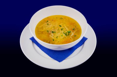 Havuçlu ve otlu sıcak tavuk çorbası. Mavi arkaplanda beyaz bir plakaya yakın çekim.