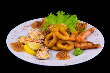 Bol bol kızarmış deniz ürünleri atıştırmalığı. Midye dolması, kalamar halkası, deniz kokteyli, limonlu kaplan karidesi. Siyah arkaplanda beyaz bir plakaya yaklaş.