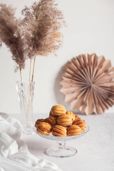 Russian traditional homemade cookies Nuts with condensed milk on glass stand on background of paper decor and reeds in vase White background, selective focus.