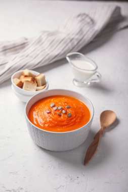 Beyaz arka planda ekmek kırıntıları, krema ve tohumlarla kabak çorbası püresi..