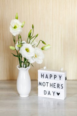 Light box with lettering Happy Mother's Day, white flowers Eustoma or Lisianthus in vase on wooden background.