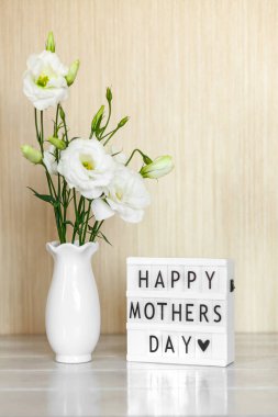Light box with lettering Happy Mother's Day, white flowers Eustoma or Lisianthus in vase on wooden background.