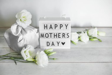 Anneler Günü 'nün kutlu olsun yazılı ışık kutusu Furoshiki tekniğinde ipek kumaşa sarılı hediye kutusu Eustoma' nın açık tahta arka planda fotokopi alanı olan beyaz çiçekleri. Sıfır Atık Yaşam Konsepti