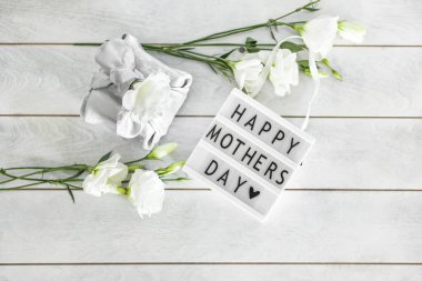 Anneler Günü 'nün kutlu olsun yazılı ışık kutusu Furoshiki tekniğinde ipek kumaşa sarılı hediye kutusu Eustoma' nın açık tahta arka planda fotokopi alanı olan beyaz çiçekleri. Sıfır Atık Yaşam Konsepti