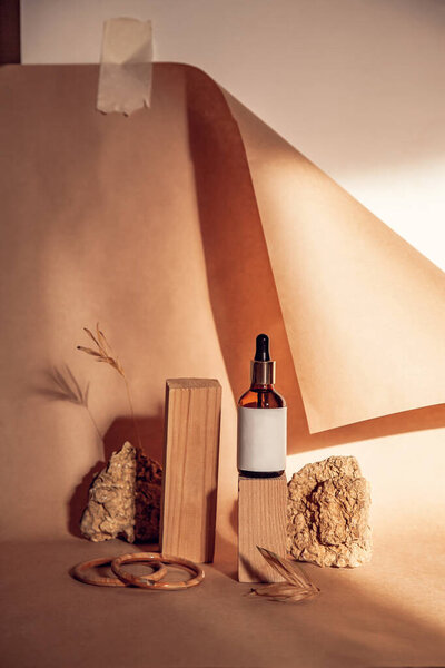 Современный натюрморт чистый макет с бутылкой сыворотки на пьедесталах с натуральными материалами на фоне ремесленной бумаги. Пустые подиумы для косметических органических продуктов и другие.