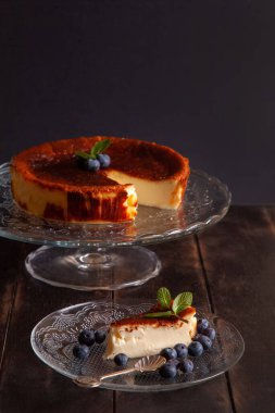 Ev yapımı Bask peynirli kek, krem peynirli, yumurta ve kremalı ekmek kırıntısı. Koyu arkaplanda yabanmersini ve nane yapraklı bir tabakta bir dilim cheesecake..