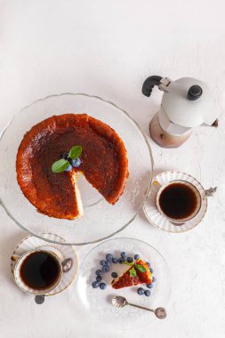 Ev yapımı Bask peyniri, üzerinde yaban mersini ve nane yaprakları olan bir tabakta, kahve ve gayzer kahve makinesi polisi düz bir görünüm sergiliyordu..