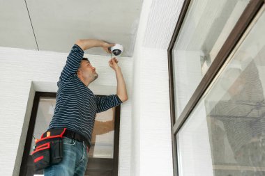 Adam merdiven üzerinde duruyor ve inşaat halindeki özel bir eve güvenlik kamerası yerleştiriyor..