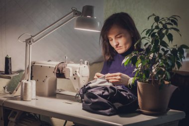 Terzi kadın elbise dikiyor. Atölyesindeki dikiş makinesinde kadife kumaştan yapılmış şık bir ceket..