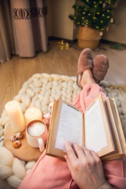 Kürk terlikli bir kadın kalın iplikten yapılmış bir battaniyeye uzanıyor, kitap okuyor, ışıkları olan bir Noel ağacının arka planında kapuçino içiyor. Umutsuzluk ve rahatlık atmosferi
