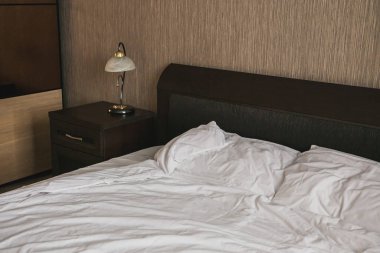 Beyaz çarşaflı yatak odası, komodin ve lamba..