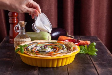 Kabak, patlıcan, havuç, dolma biber, silikon kabuklu fesleğen ile sebzeli turta pişirme işlemi. Kadın pastaya krema döker.
