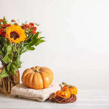 Sonbahar havası. Ahşap arka planda sıcacık bir sonbahar yaşamı. Bir buket ayçiçeği, balkabağı, yün kazaklar, akçaağaç yaprakları ve hurma. Boşluğu kopyala