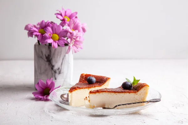 Ev yapımı Bask peyniri dilimleri hafif arka planda yaban mersini ve nane yapraklı bir tabakta yanmış cheesecake.