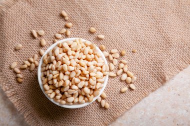 Organik çam fıstığı bir kase içinde jüt peçetenin üzerinde arka planda açık bir zemin üzerinde düz bir şekilde yatıyordu.