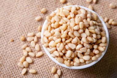 Organik çam fıstığı bir kase içinde jüt peçetenin üzerinde arka planda açık bir zemin üzerinde düz bir şekilde yatıyordu.