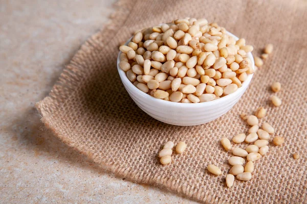 Organic Pine nuts in a bowl on a jute napkin on a light background close up