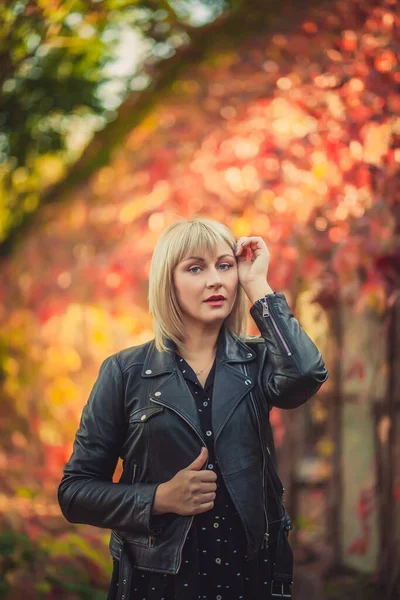 Young woman with bob haircut and fringe in a black leather jacket is standing in an abandoned greenhouse in autumn. Staged photo shoot