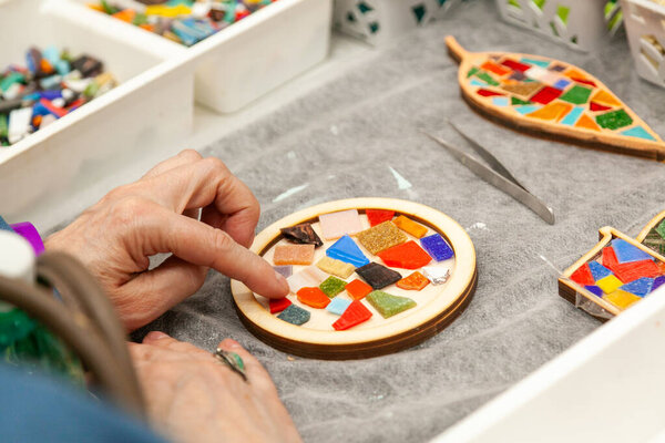 Master class on making mosaic panels. Close-up of the hands of a student of an adult woman arranging a composition