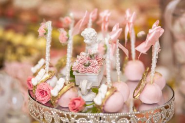 Açık büfe alanındaki düğün şekerleme barında leziz tatlılar: meleklerle süslenmiş kek çubukları ve cameo ve taze gül tomurcukları.