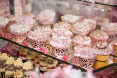 Açık büfe alanındaki düğün şekerleme barında lezzetli tatlılar: meleklerle süslenmiş muffinler, şeker goncaları ve altın sarısı boyalar.