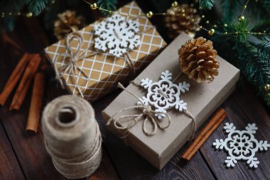 Yaratıcı sıfır israf Noel konsepti, sicimle bağlanmış el yapımı hediye kutuları, altın köknar kozalakları ve ahşap kar taneleri ve tarçın çubukları.