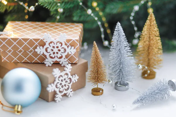 Vánoční dárky a dárkové krabice zabalené v kraftovém papíru na dřevěném stole se zlatými a stříbrnými ozdobnými vánočními stromky, větvemi jedlí a dekoracemi. Nový rok, vánoční koncept. — Stock fotografie