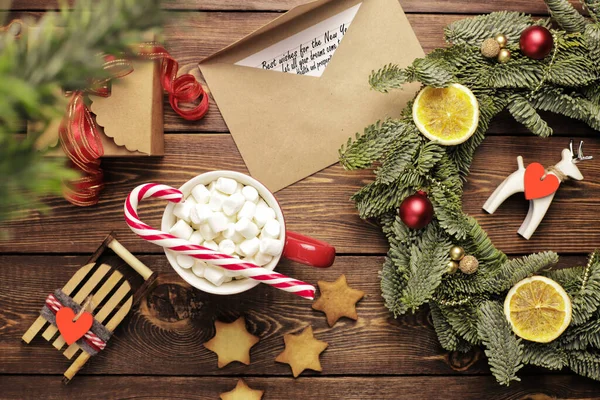 Christmas wreath, gift, coffee mug with marshmallows, envelope and homemade cookies and various Christmas decorations on the wooden table. Rustic christmas wreath, flat lay.