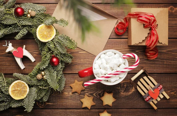 Vánoční věnec, dárek, kávový hrnek s marshmallows, obálka a domácí sušenky a různé vánoční ozdoby na dřevěném stole. Rustikální vánoční věnec, plochý ležel. — Stock fotografie
