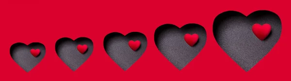 黒い表面に小さな心を持つバナーは、大きな心の中に赤い段ボールに刻まれています。愛の幸福と献身の象徴です。ハッピーバレンタインデー。郵便はがき. — ストック写真