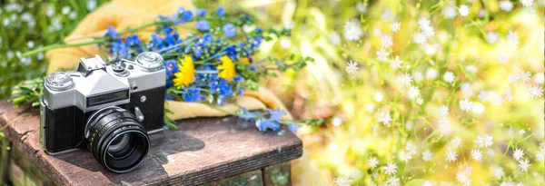 Ramo de flores silvestres y la cámara fotográfica de película retro en una silla de madera en el jardín de verano. — Foto de Stock