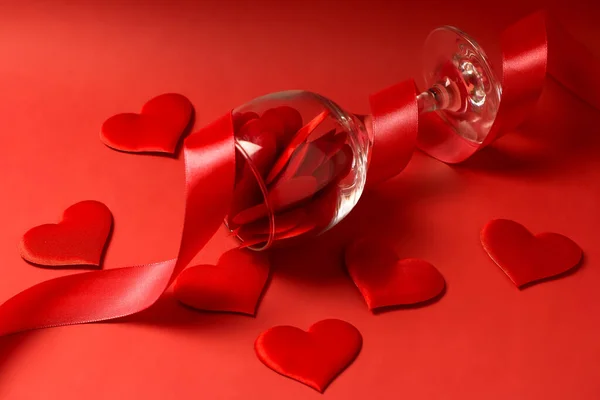 A glass full of satin hearts with red ribbon on a red background. Valentines day concept. Happy Valentines Day. Postcard. Copy space.