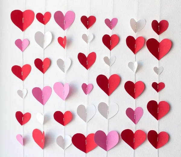 Paper hearts of red, white and pink colors, strung on threads, hang on a white wall. Decoration for Valentines Day. Valentines Day concept — Stock Photo, Image