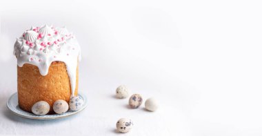  Traditional homemade Easter cake, decorated with glaze and pastry sprinkles on a blue plate on a white table with quail eggs. Happy Easter. 