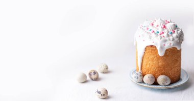  Traditional homemade Easter cake, decorated with glaze and pastry sprinkles on a blue plate on a white table with quail eggs. Happy Easter. 