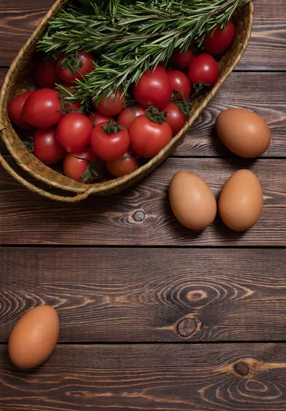Tomates frescos, pepinos, alguns ramos de alecrim em uma cesta de vime, ovos de frango em uma mesa de madeira. Colheita. Produto agrícola. — Fotografia de Stock