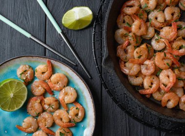 Mavi bir porselen tabakta sarımsakla kızartılmış karidesler ve siyah ahşap bir masada bir dilim kireç dilimli siyah bir demir tavada. Üst görünüm