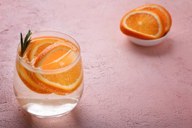 Dilimlenmiş portakallı limonata ve pembe bir masada bir tutam biberiye..