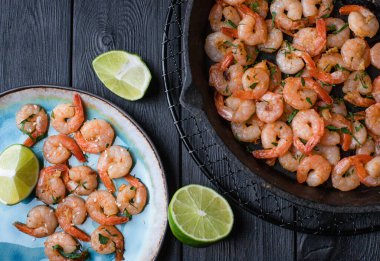 Mavi bir porselen tabakta sarımsakla kızartılmış karidesler ve siyah ahşap bir masada bir dilim kireç dilimli siyah bir demir tavada. Üst görünüm