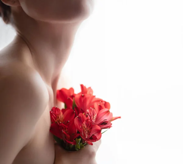 A naked girl in defocus holds a bouquet of red alstroemeria. Front view. Selective focus. — Stock Photo, Image