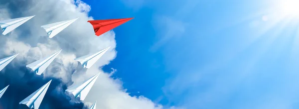 Red Paper Airplane Leading Fleet Of Small White Planes Away From Approaching Storm Toward Blue Sky And Sun - Leadership Concept