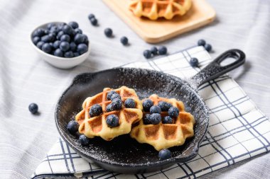 Ev yapımı waffle yaban mersini ve tavaya benzeyen bir tabakta krema..