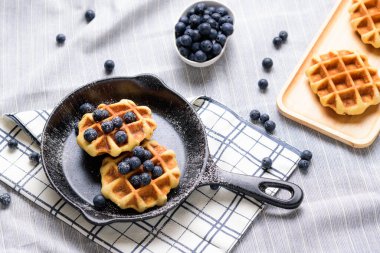 Ev yapımı waffle yaban mersini ve tavaya benzeyen bir tabakta krema..