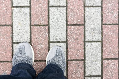 Genç Adam 'ın ayaklarının üst görüntüsü gri ayakkabılar veya spor ayakkabıları ve kırmızı ve beyaz beton blokta kot pantolon giyiyor