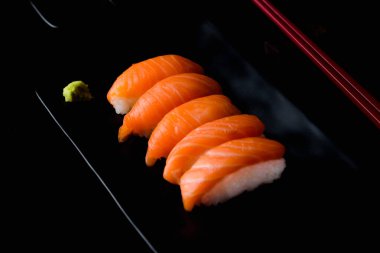 Siyah tabakta yeşil wasabi ve siyah zemin üzerinde shoyu soslu somon balığı.