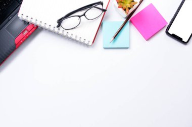 Üst görünüm ya da düz görünüm çalışma alanı kopya alanı ile dizüstü bilgisayar, kalem, defter, gözlük, yapışkan not ve cep telefonu beyaz masa arka planında veya izole edilmiş