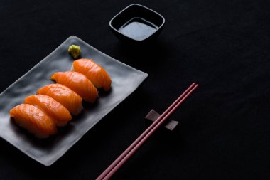 Siyah tabakta yeşil wasabi ve siyah zemin üzerinde shoyu soslu somon balığı.