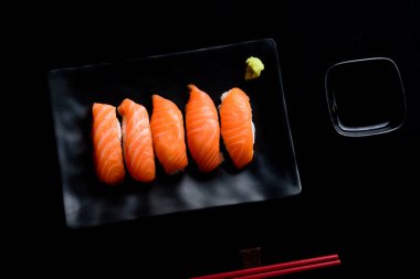 Siyah tabakta yeşil wasabi ve siyah zemin üzerinde shoyu soslu somon balığı.